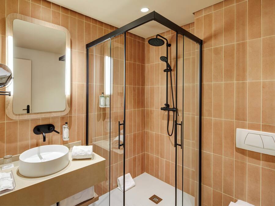 Een moderne badkamer met een douchecabine van glas, een rond wastafel, een spiegel en een haardroger.