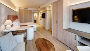 A modern hotel room with a sofa, a wooden coffee table, a TV, and a small dining area. - Sercotel Hotel Pozuelo (Pozuelo de Alarcon)