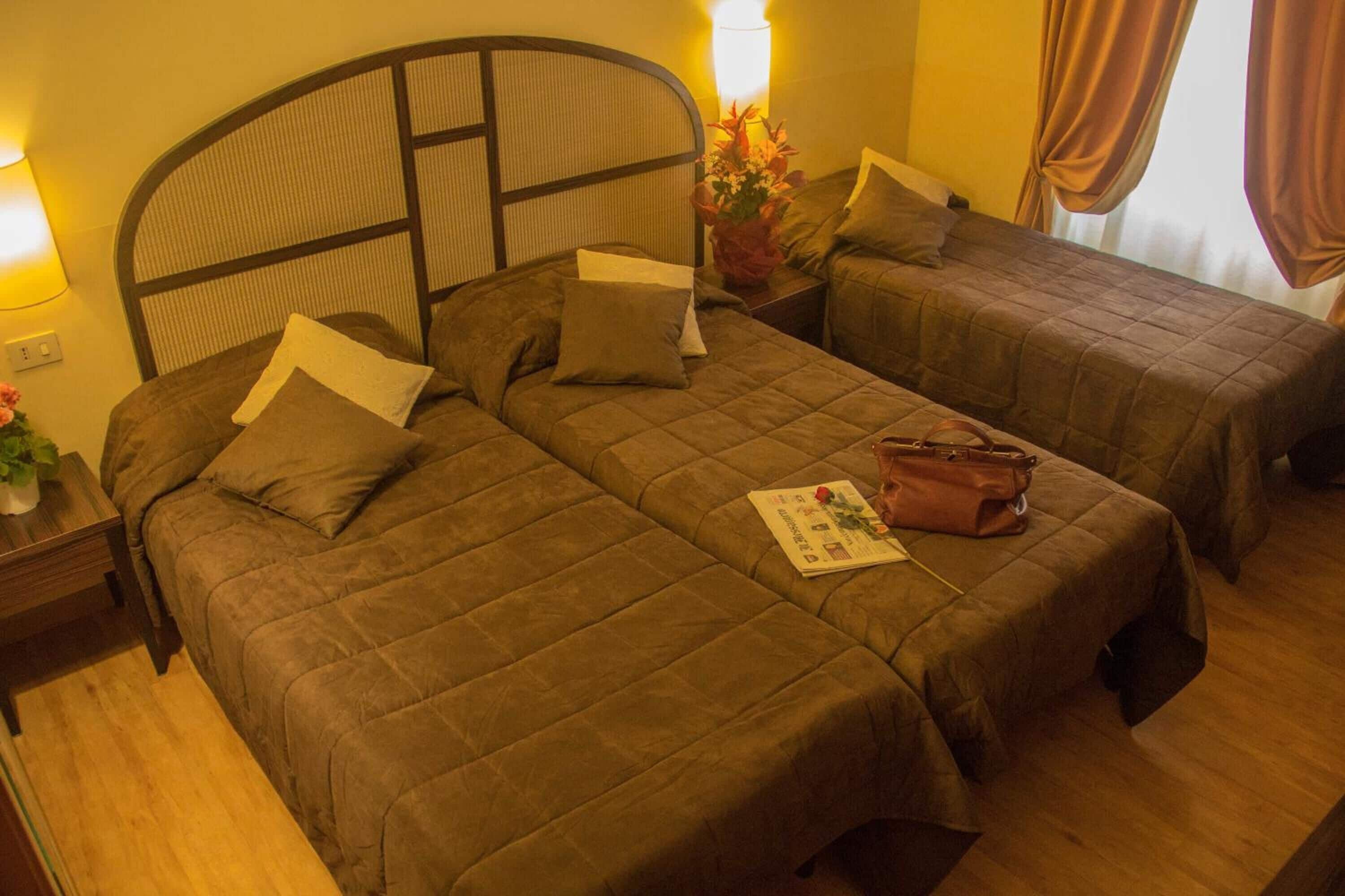 A hotel room with two beds, each with a headboard, a bedside table, and a lamp.