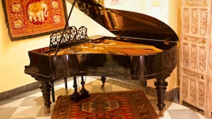 A grand piano with intricate carvings, a decorative rug, and a traditional cabinet in a well-lit room. - Hotel Novecento (Rome)