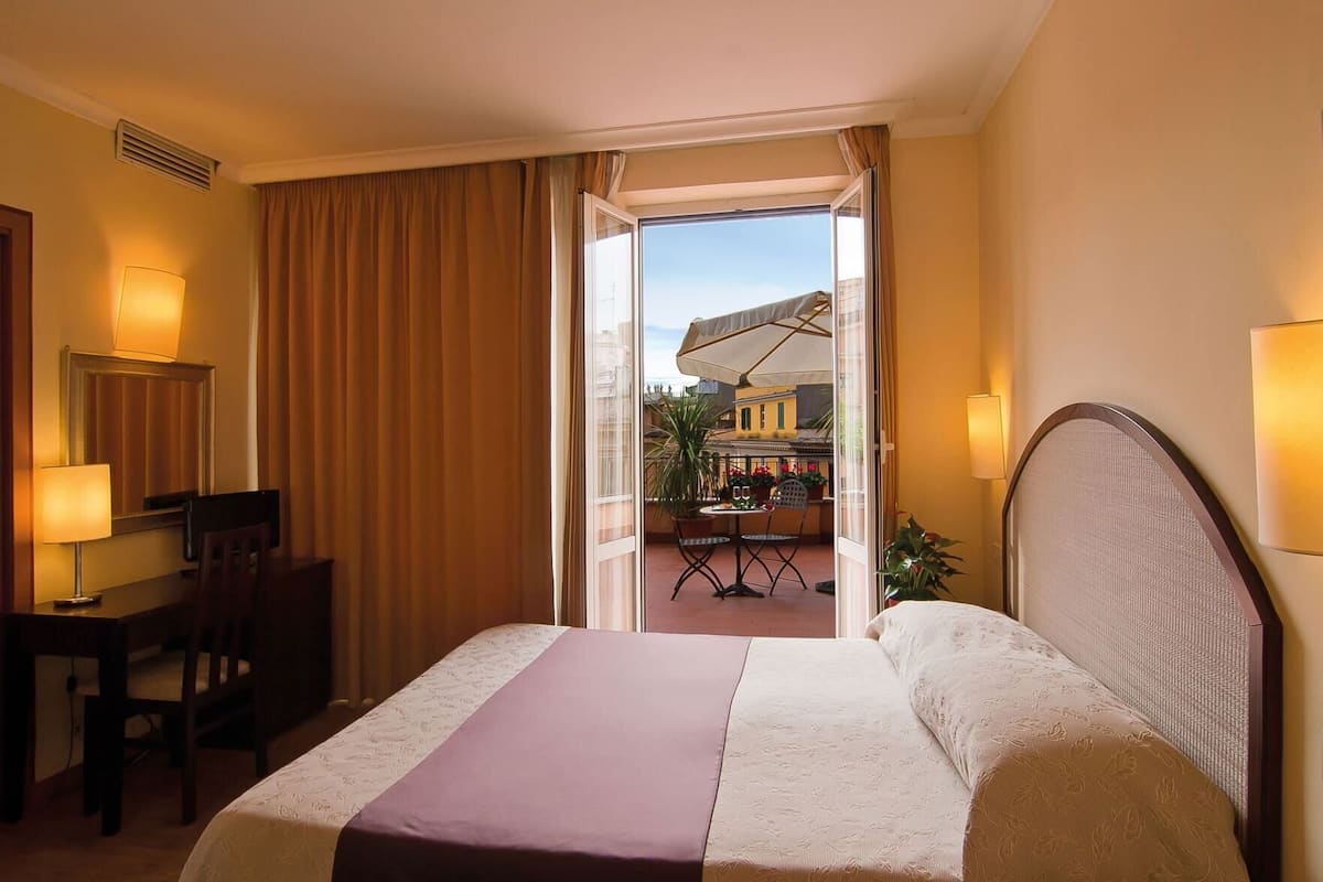 Een hotelkamer met een bed, bureau, stoel en uitzicht op het terras.