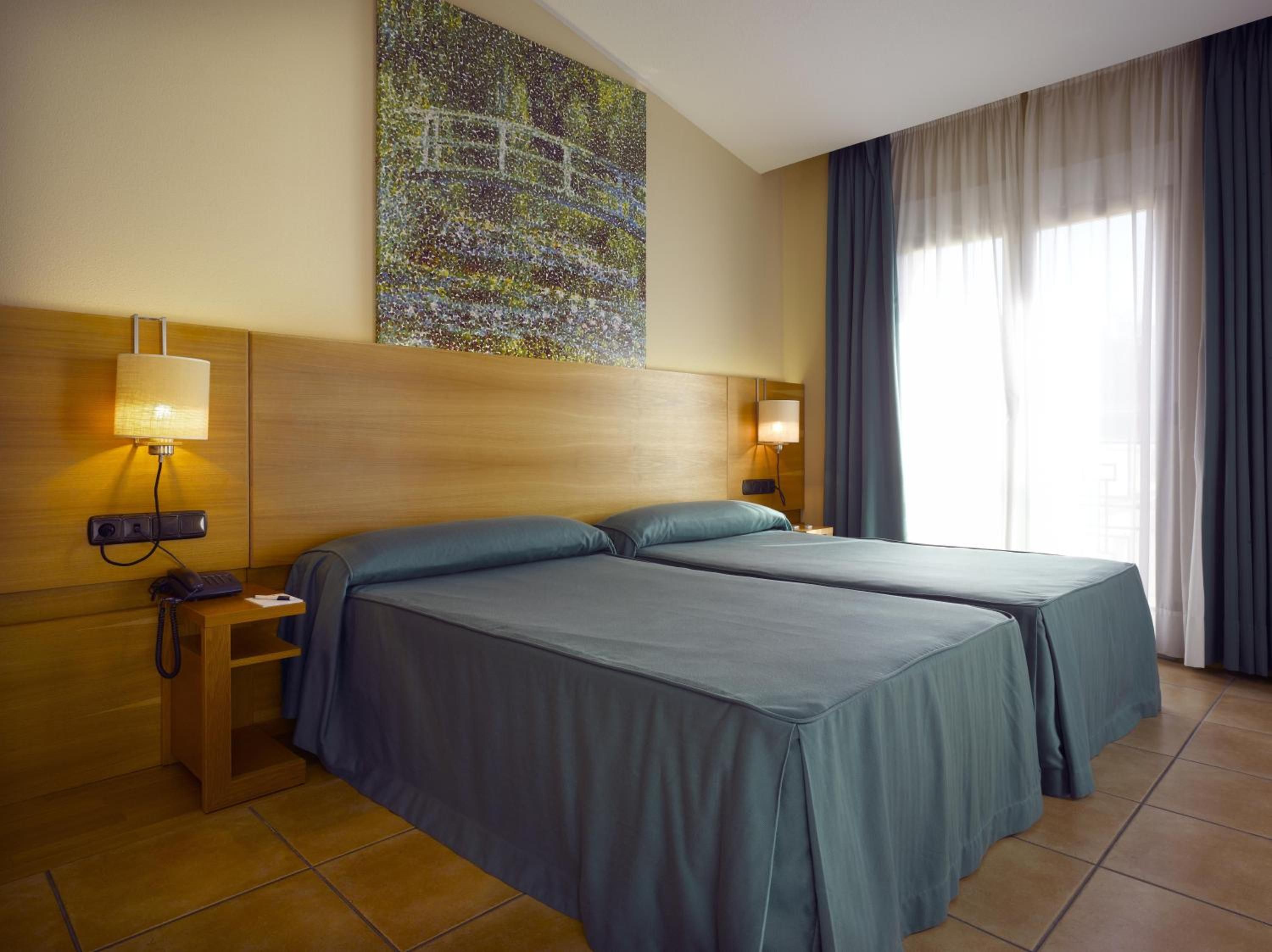 A hotel room with two beds, a nightstand, a lamp, and a painting on the wall.