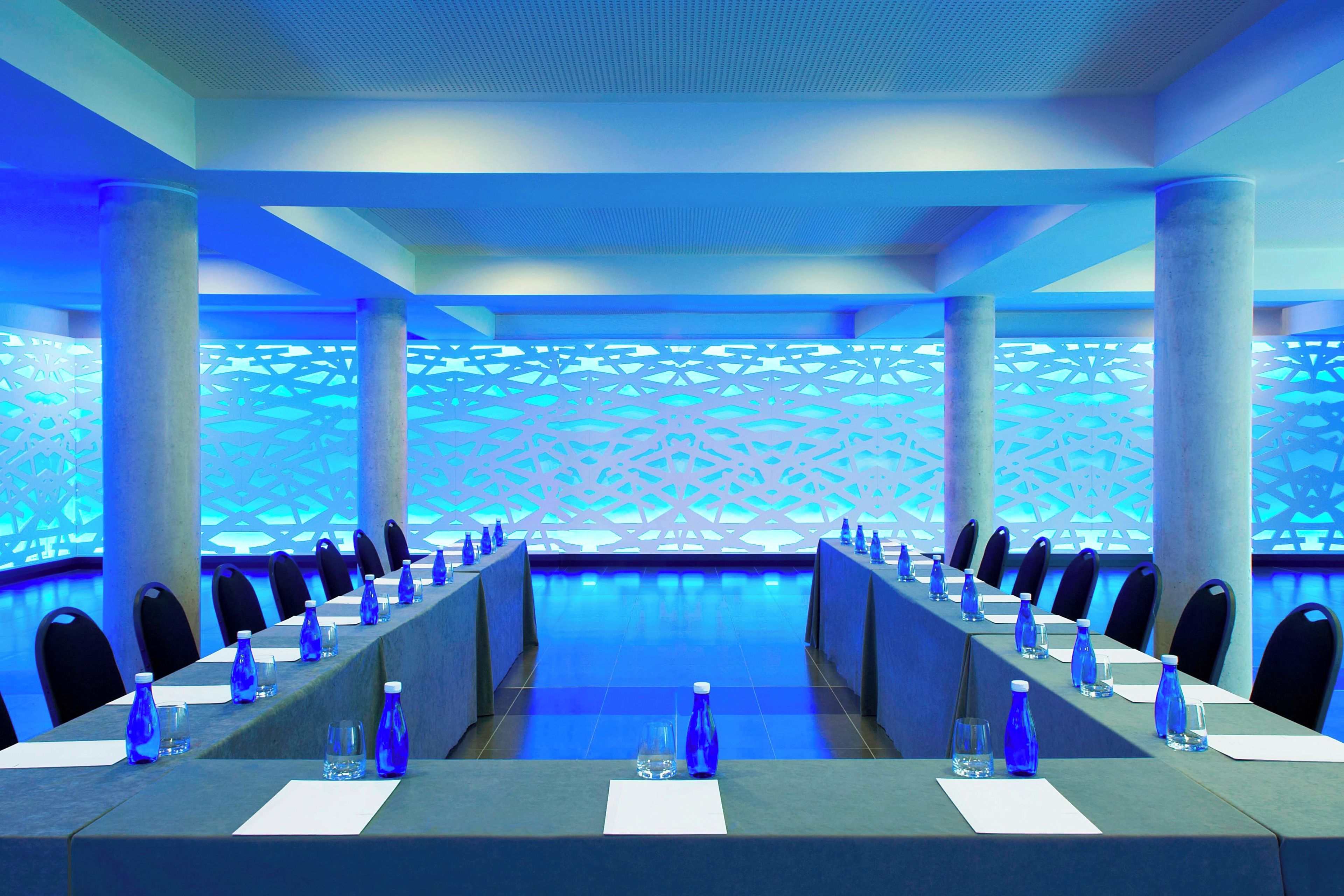 Un salón de conferencias con una larga mesa, sillas y botellas de agua.