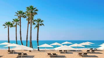 Una playa con palmeras, sombrillas blancas y sillones de playa.