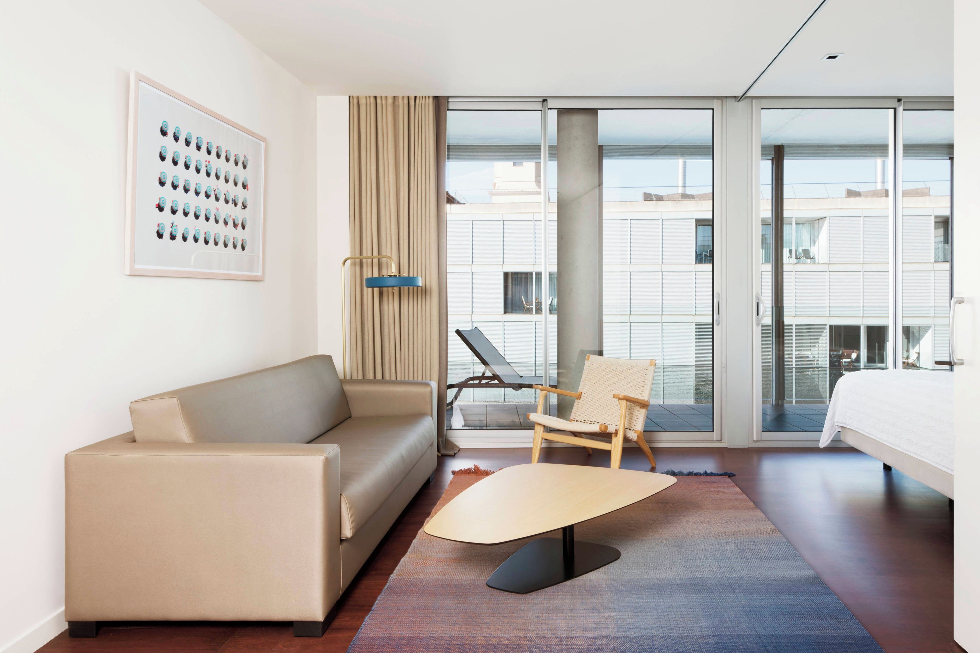 Habitación de hotel con sofá, una silla, cama, una mesita de centro y un ventanal con vista a edificios.