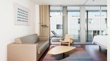 Habitación de hotel con sofá, una silla, cama, una mesita de centro y un ventanal con vista a edificios.