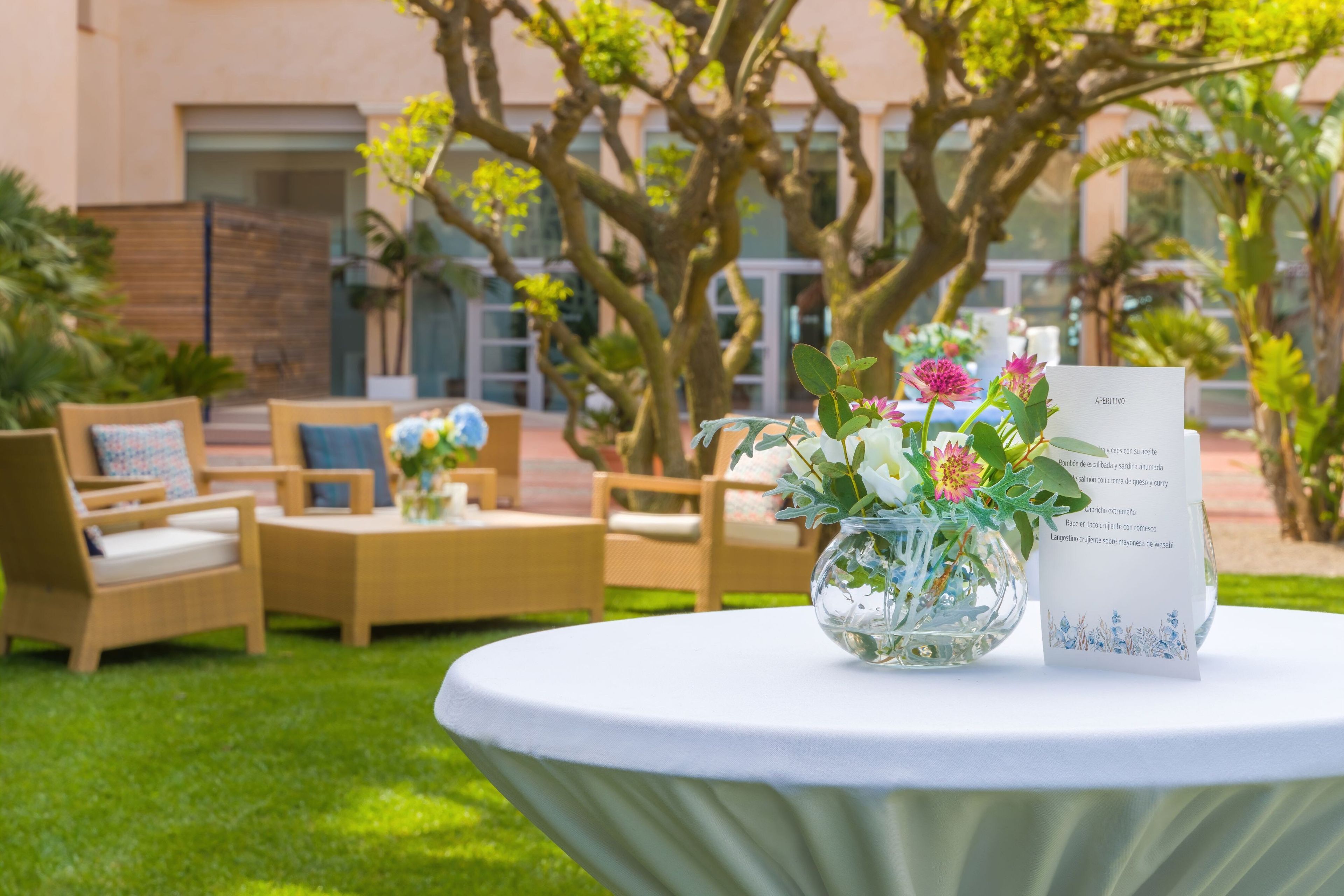 Une table ronde recouverte d’une nappe blanche, un vase en verre avec des fleurs et un menu placé sur le côté droit.