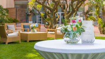 Une table ronde recouverte d’une nappe blanche, un vase en verre avec des fleurs et un menu placé sur le côté droit.