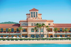 A hotel with a poolside area, palm trees, and a clear blue sky.