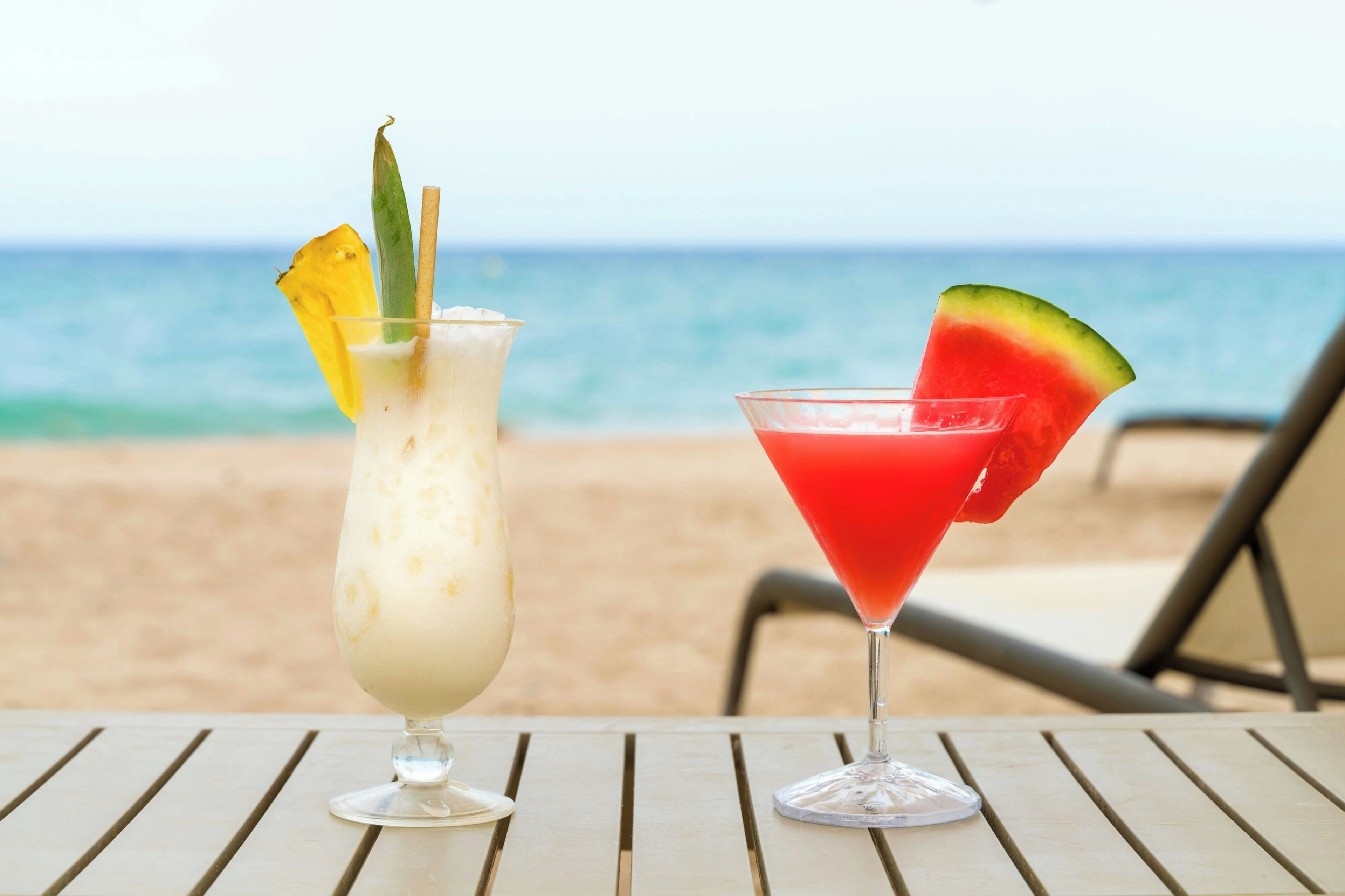 Two drinks on a table with a beach and ocean in the background.