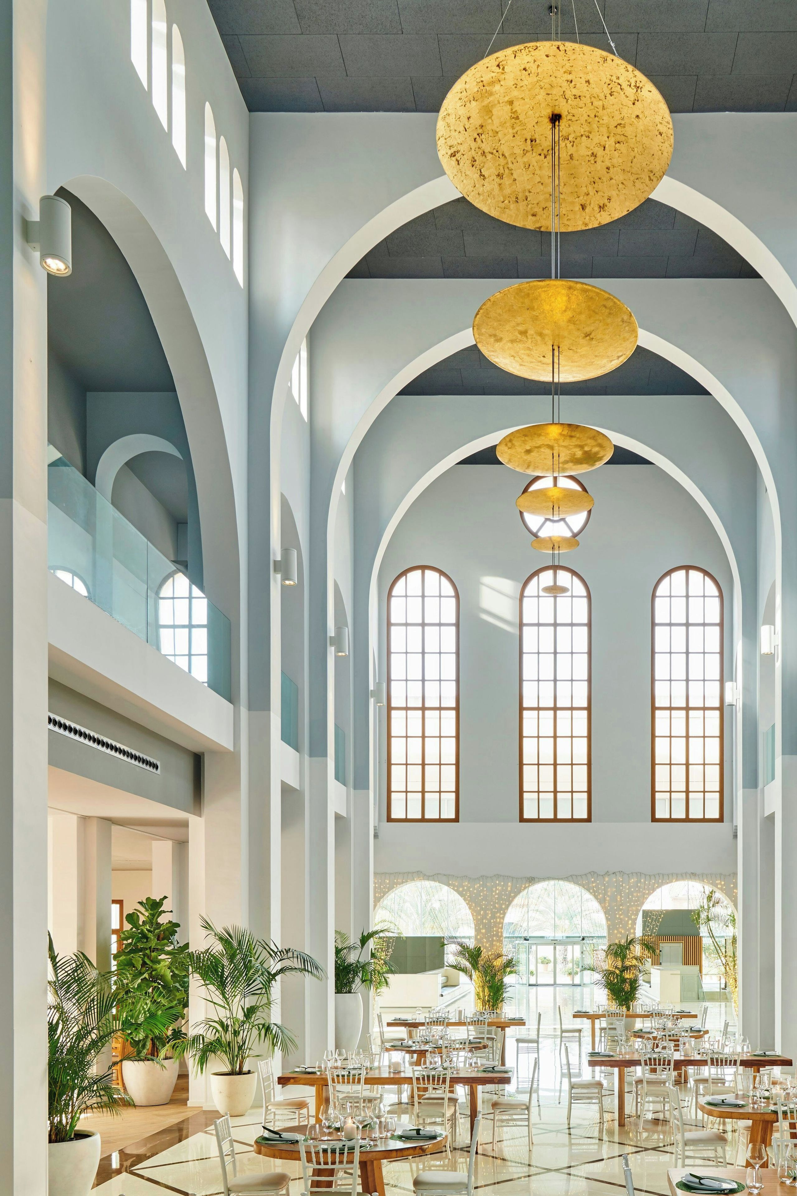 Um hall amplo com pé direito alto, janelas em arco e um lustre central.