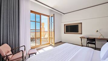 Habitación de hotel con una cama grande, un escritorio, una silla y un balcón con vista al mar.