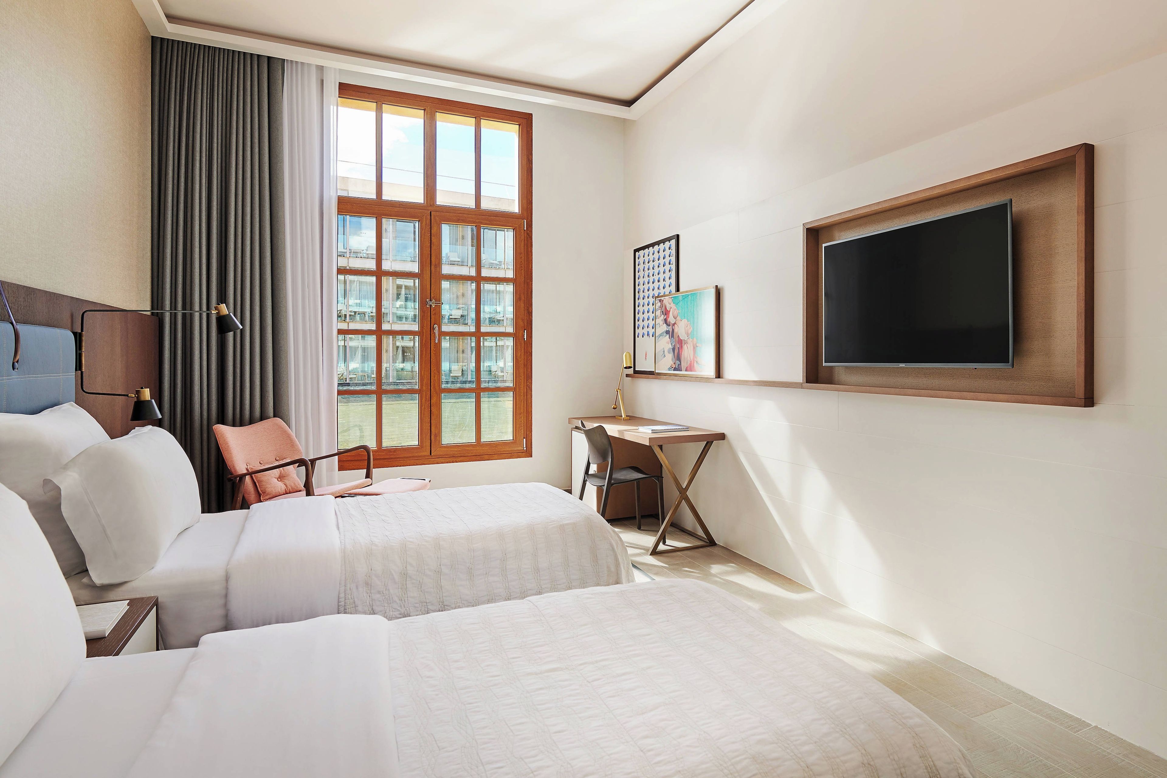 Une chambre d’hôtel avec deux lits, un bureau, une chaise, une télévision et une fenêtre avec des rideaux.