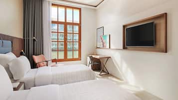 Une chambre d’hôtel avec deux lits, un bureau, une chaise, une télévision et une fenêtre avec des rideaux.