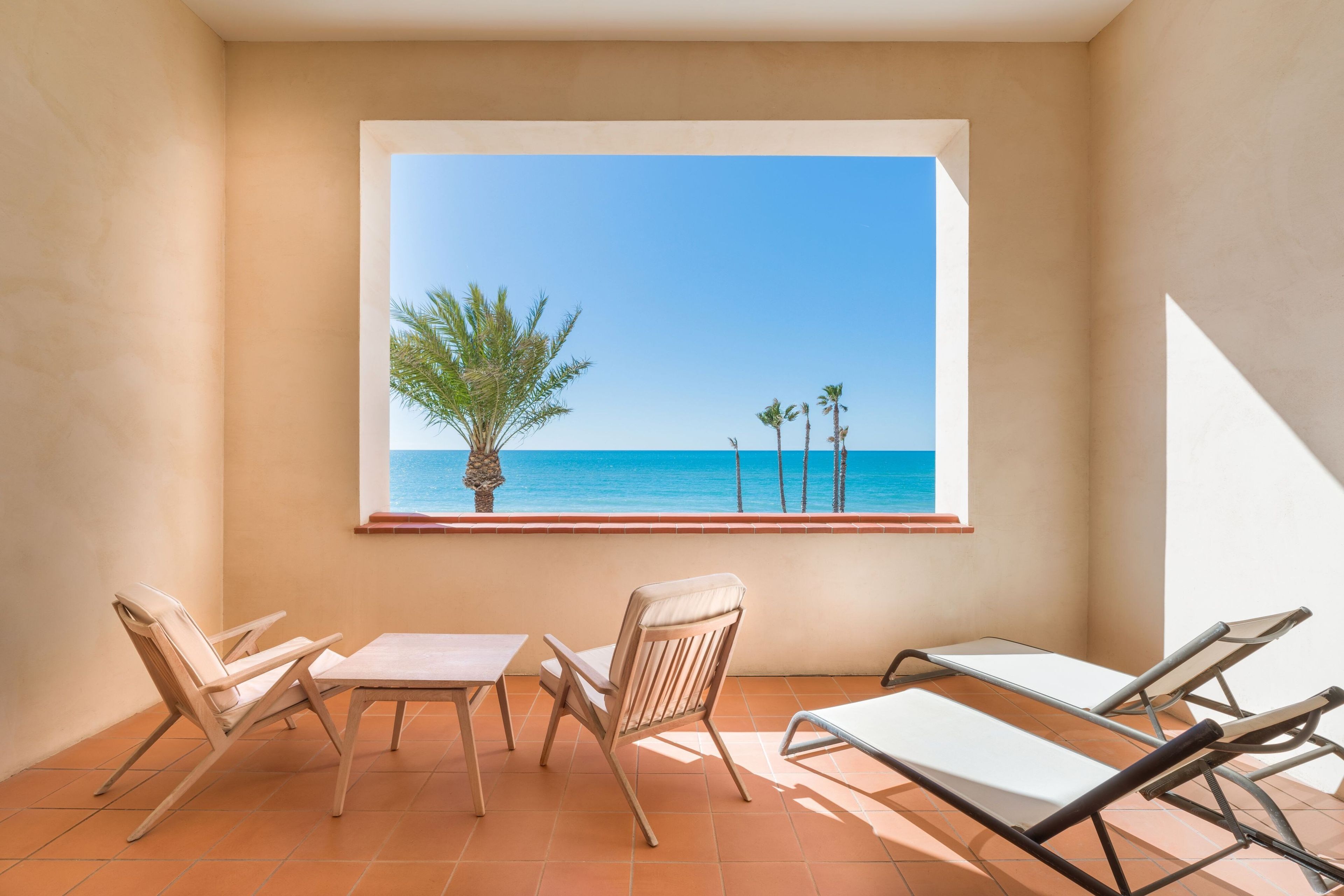 Un balcón con vistas al mar, una mesa, dos sillas y una tumbona.