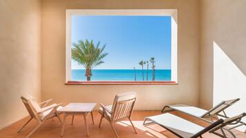 Un balcón con vistas al mar, una mesa, dos sillas y una tumbona.