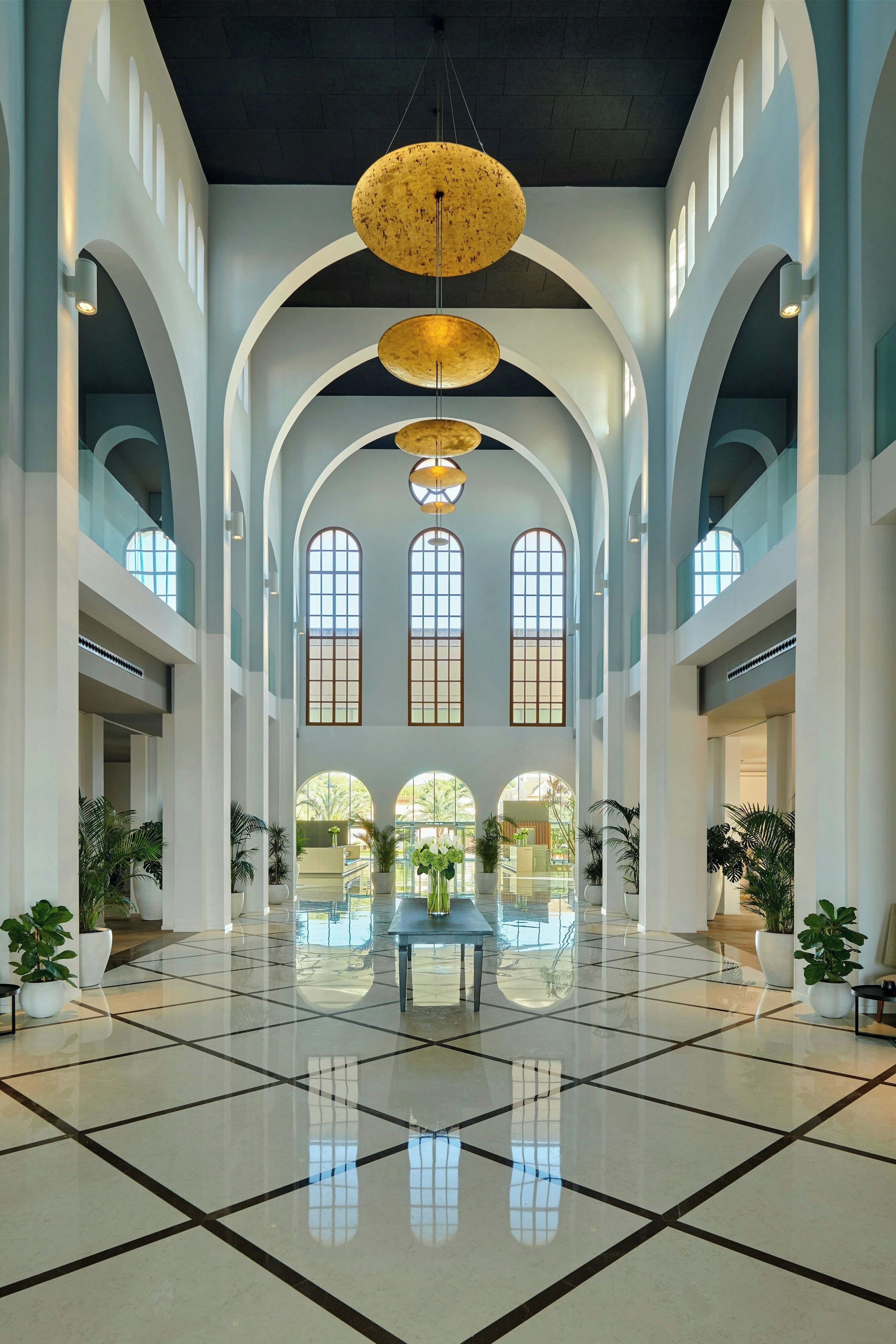 Eine großzügige Lobby mit hohen Decken, großen Bogenfenstern und einer zentral gelegenen Sitzecke.