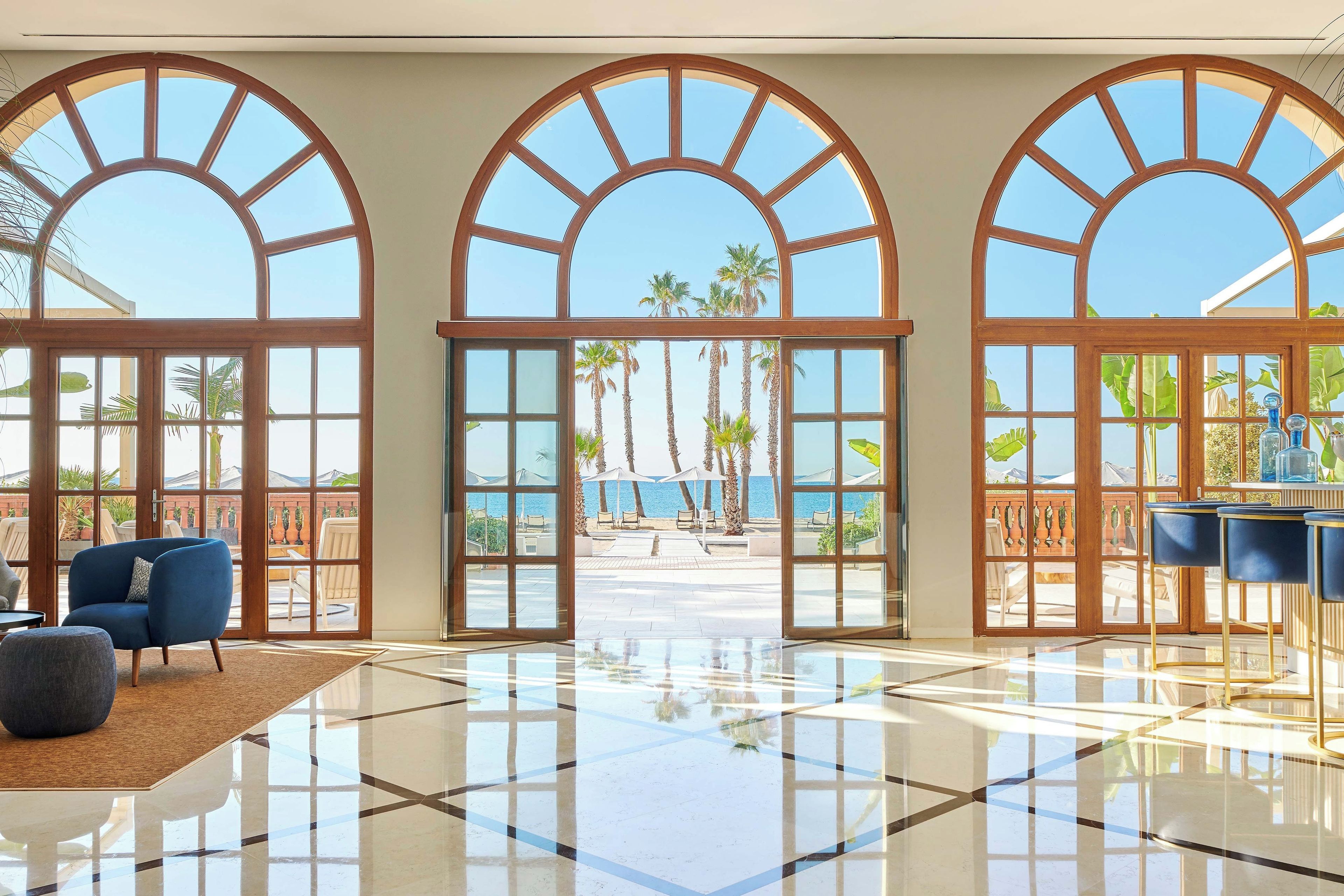 A spacious lobby with large arched windows, a polished floor, and a seating area with chairs.