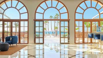 A spacious lobby with large arched windows, a polished floor, and a seating area with chairs.