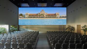 Un auditorium avec des rangées de sièges disposés face à un grand écran sur lequel est projeté un bâtiment situé sur la côte.