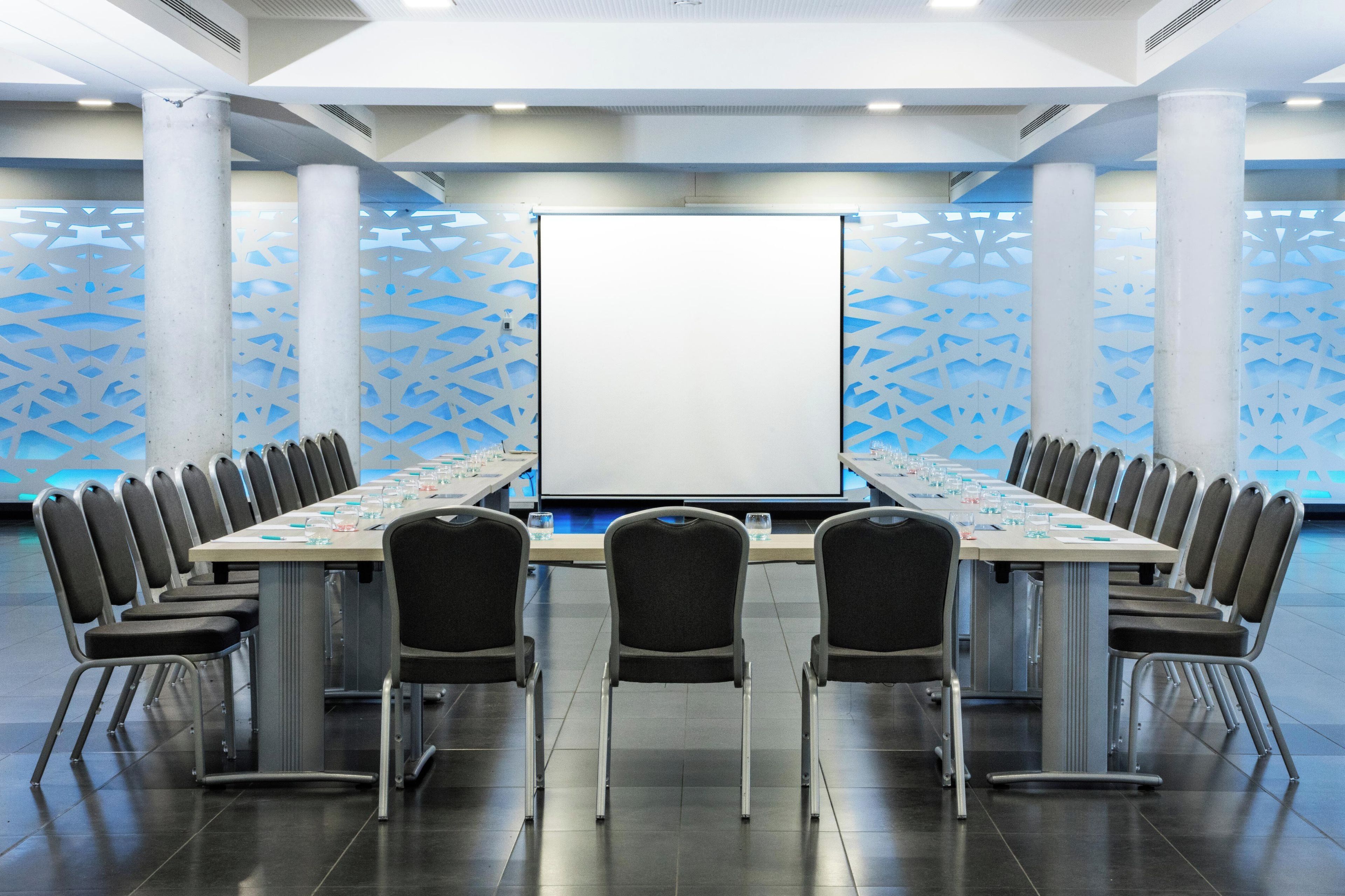 A conference room with a long table, chairs, a projector screen, and patterned walls.