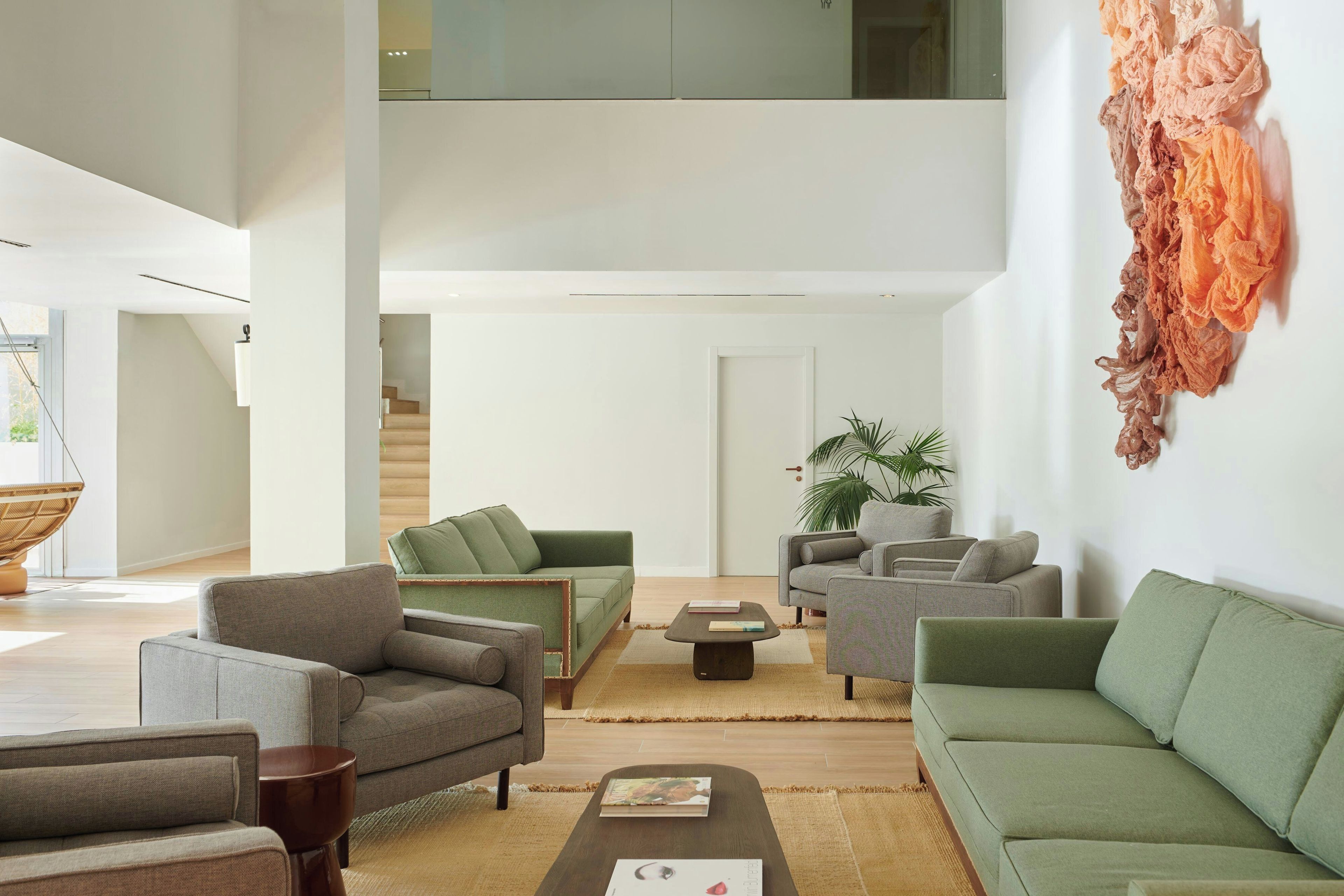 A modern living room with a green sofa, grey armchairs, and a coffee table. There is a staircase leading to an upper level.