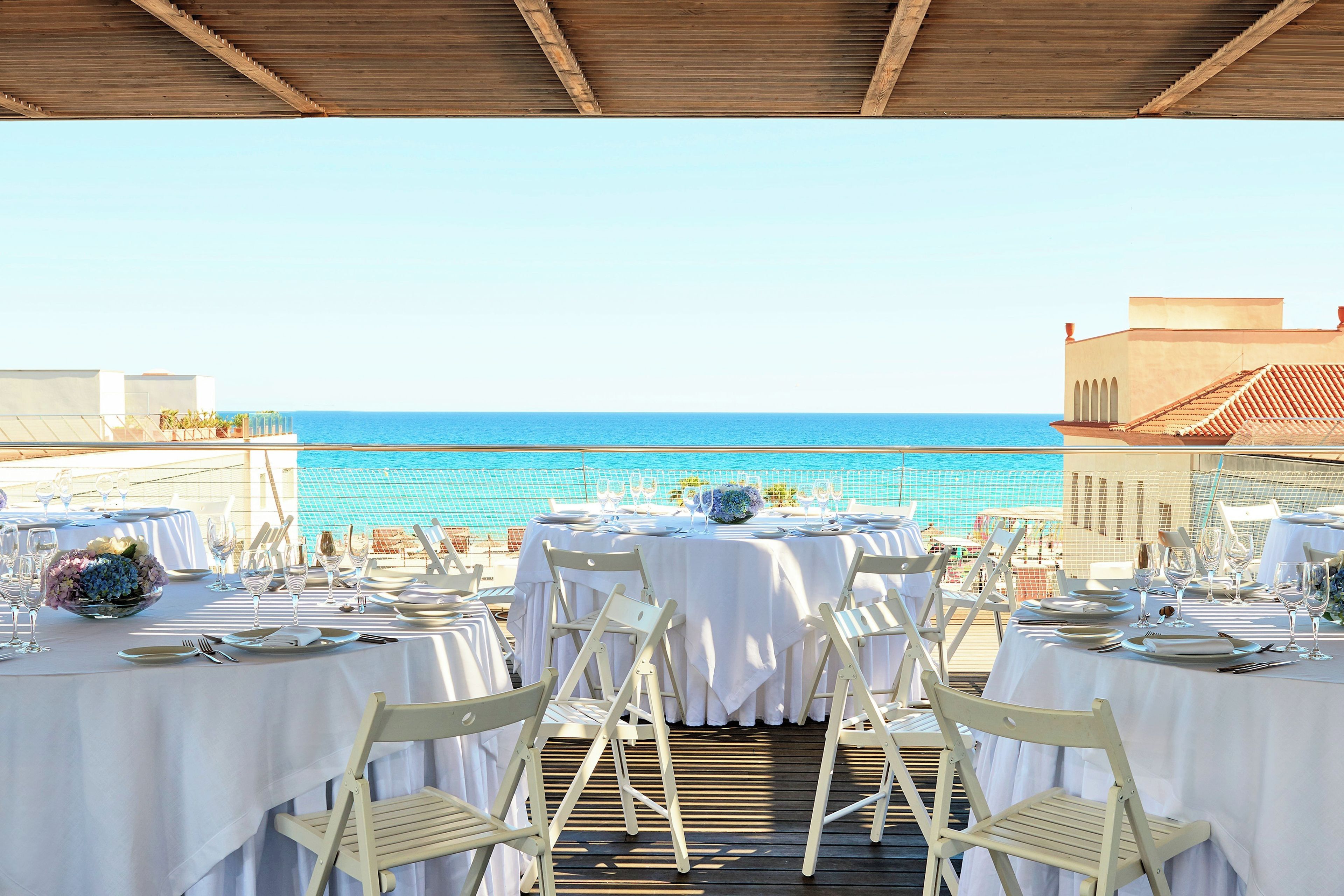 Un espacio de comedor al aire libre con mesas dispuestas para una comida, con vistas al mar.