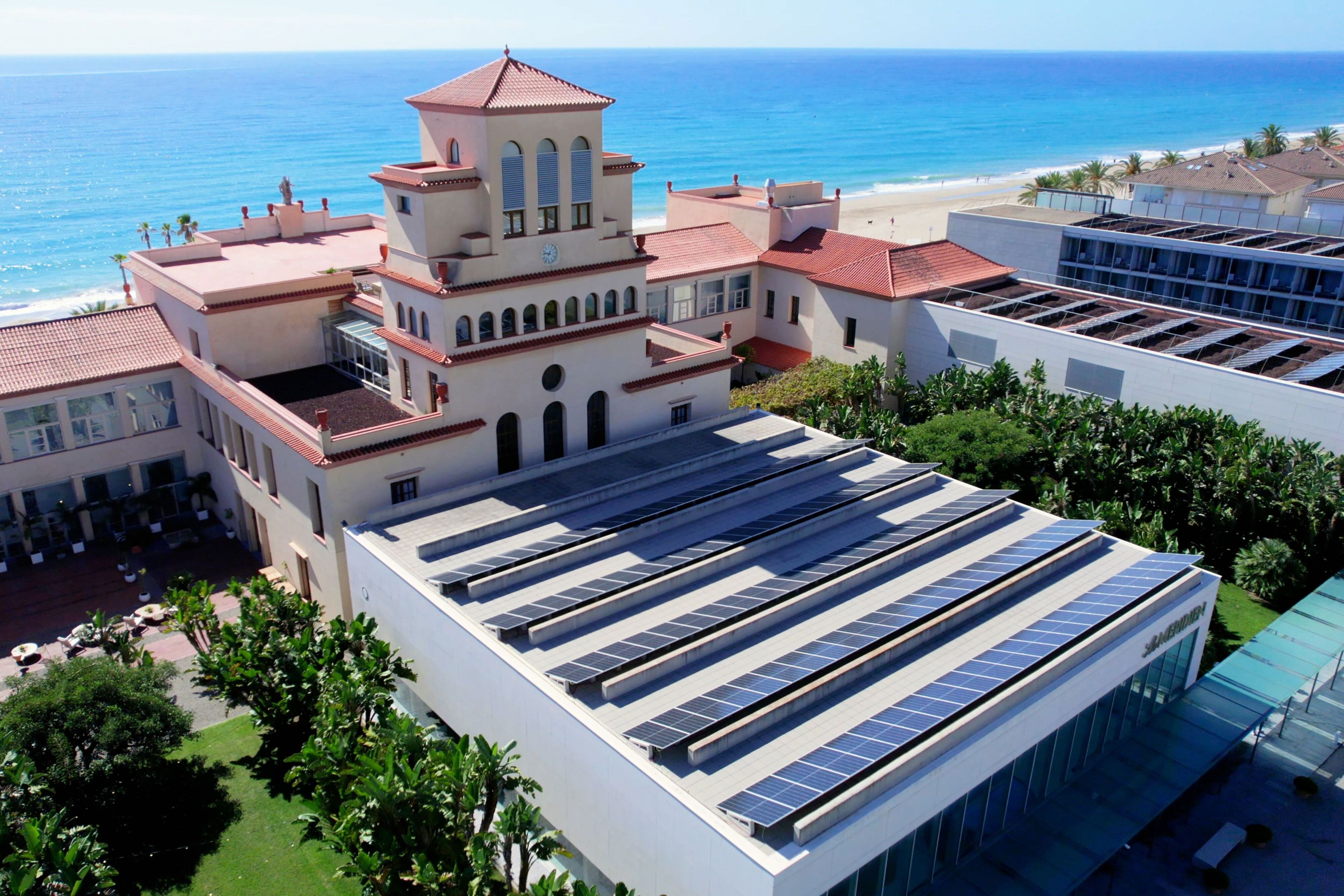Un hotel con paneles solares en la azotea, una torre central y vista al mar.