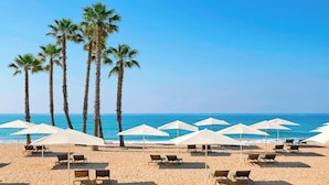 Una playa con palmeras, sombrillas blancas y sillones de playa.
