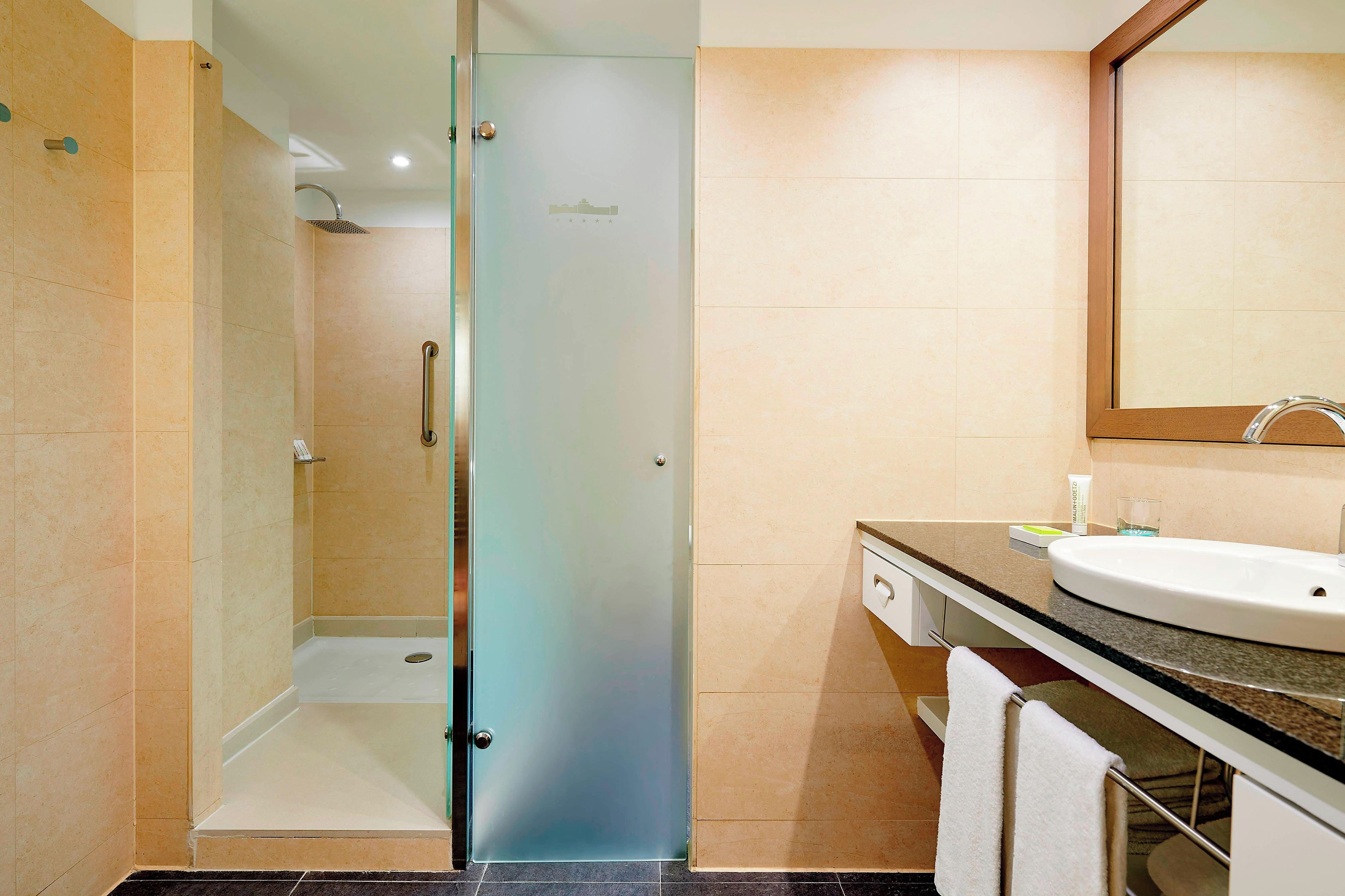 Un baño moderno con cabina de ducha de vidrio, un lavabo con espejo y un perchero para toallas.