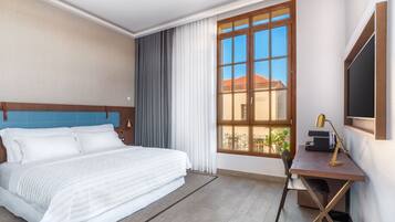 A hotel room with a bed, a desk, a chair, a window with curtains, and a TV on the wall.