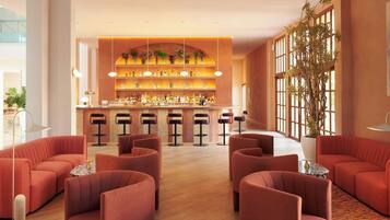 Een bar met een lange toonbank, meerdere krukken en een grote potplant.