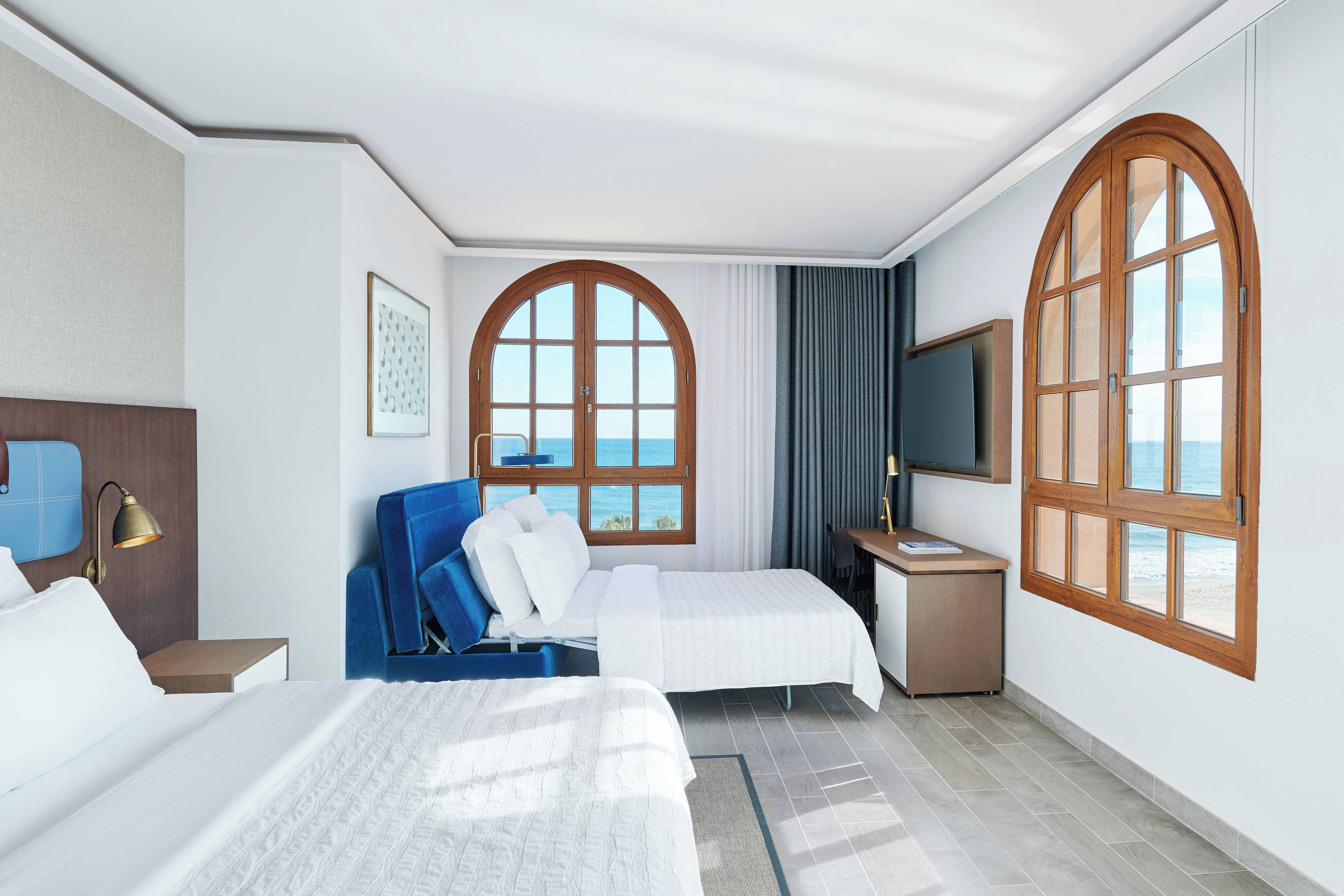 Een hotelkamer met twee bedden, een bureau, een televisie en grote ramen met uitzicht op de oceaan.