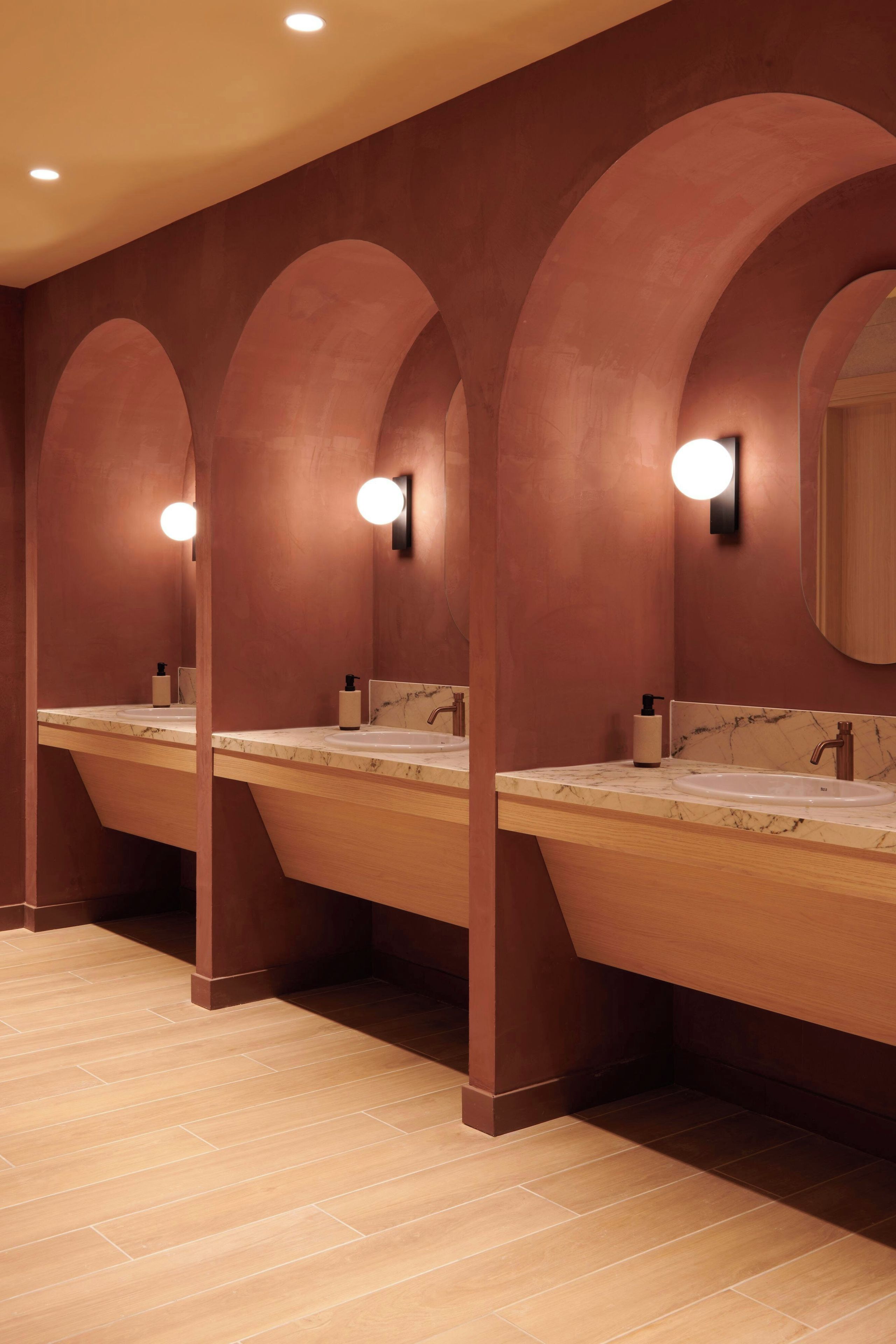 A row of wooden vanity mirrors with built-in lighting, marble countertops, and a tiled floor.