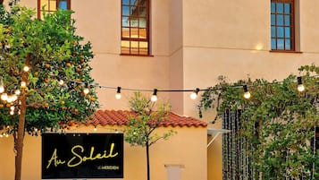 A building with a tiled roof, a sign reading "An Soleil", and rows of white chairs arranged for an event.