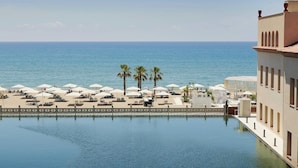 Vista a la piscina con una vista despejada del mar, palmeras y un edificio con terraza.