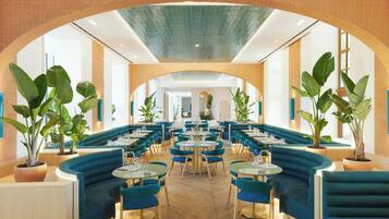 Um restaurante com assentos em azul, mesas redondas e plantas em vasos.