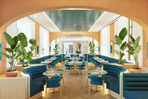 A restaurant with blue booths, round tables, and potted plants. - Le Meridien Ra Beach Hotel & Spa (El Vendrell)