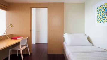 A room with a desk, chair, bed, and a door leading to another room.
