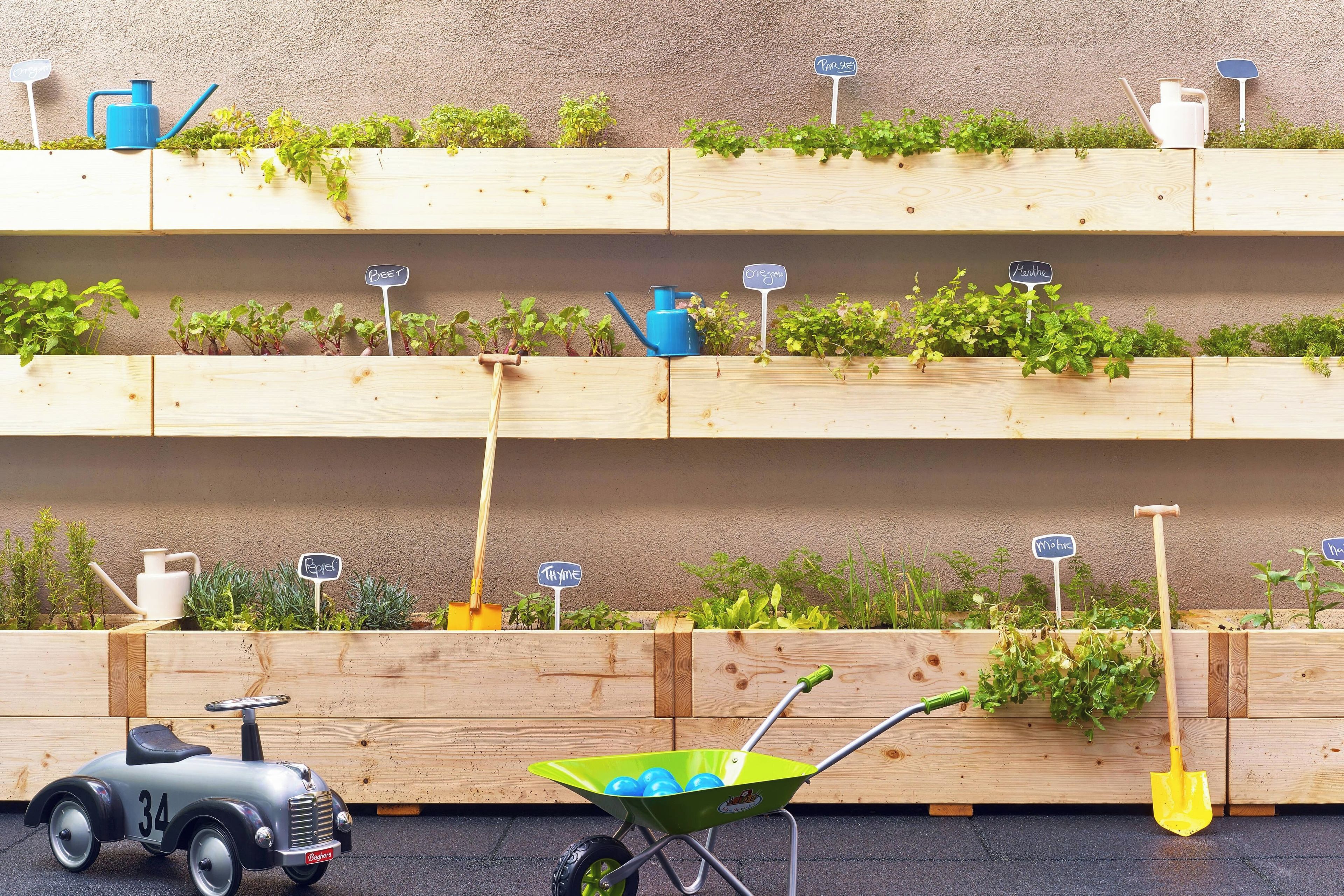 A wooden planter box with various plants and gardening tools.