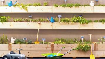 A wooden planter box with various plants and gardening tools.