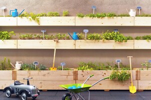 Una jardinera de madera con diversas plantas y herramientas de jardinería.