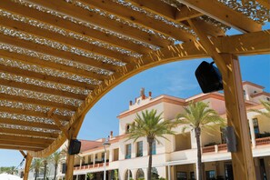 Una estructura de pérgola de madera con vista despejada a un edificio con varios balcones y palmeras.