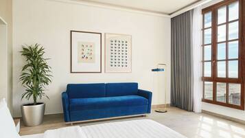 A modern room with a blue sofa, a potted plant, a bed, and a large window with a view.