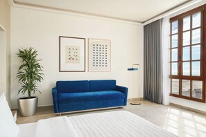 Una habitación moderna con un sofá azul, una planta en maceta, una cama y un ventanal con vistas.