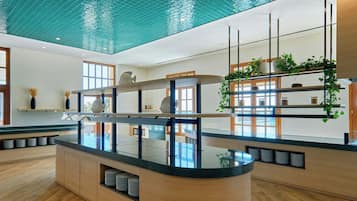 Un moderno vestíbulo de hotel con un mostrador de recepción central, un ventanal grande y un techo con superficie reflectante.