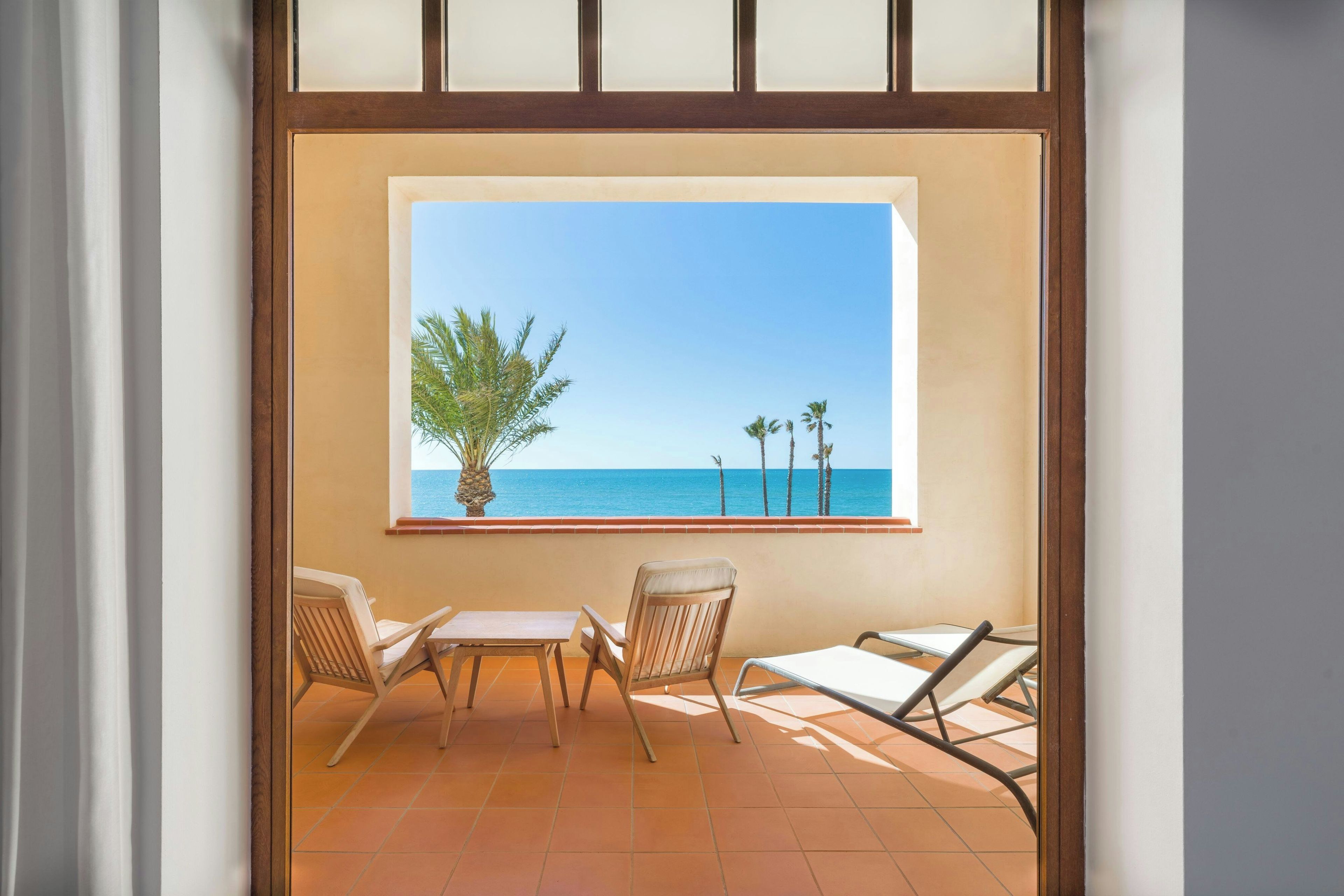 A balcony with a view of the sea, two chairs, and a small table.