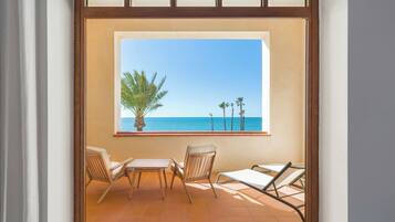 A balcony with a view of the sea, two chairs, and a small table.