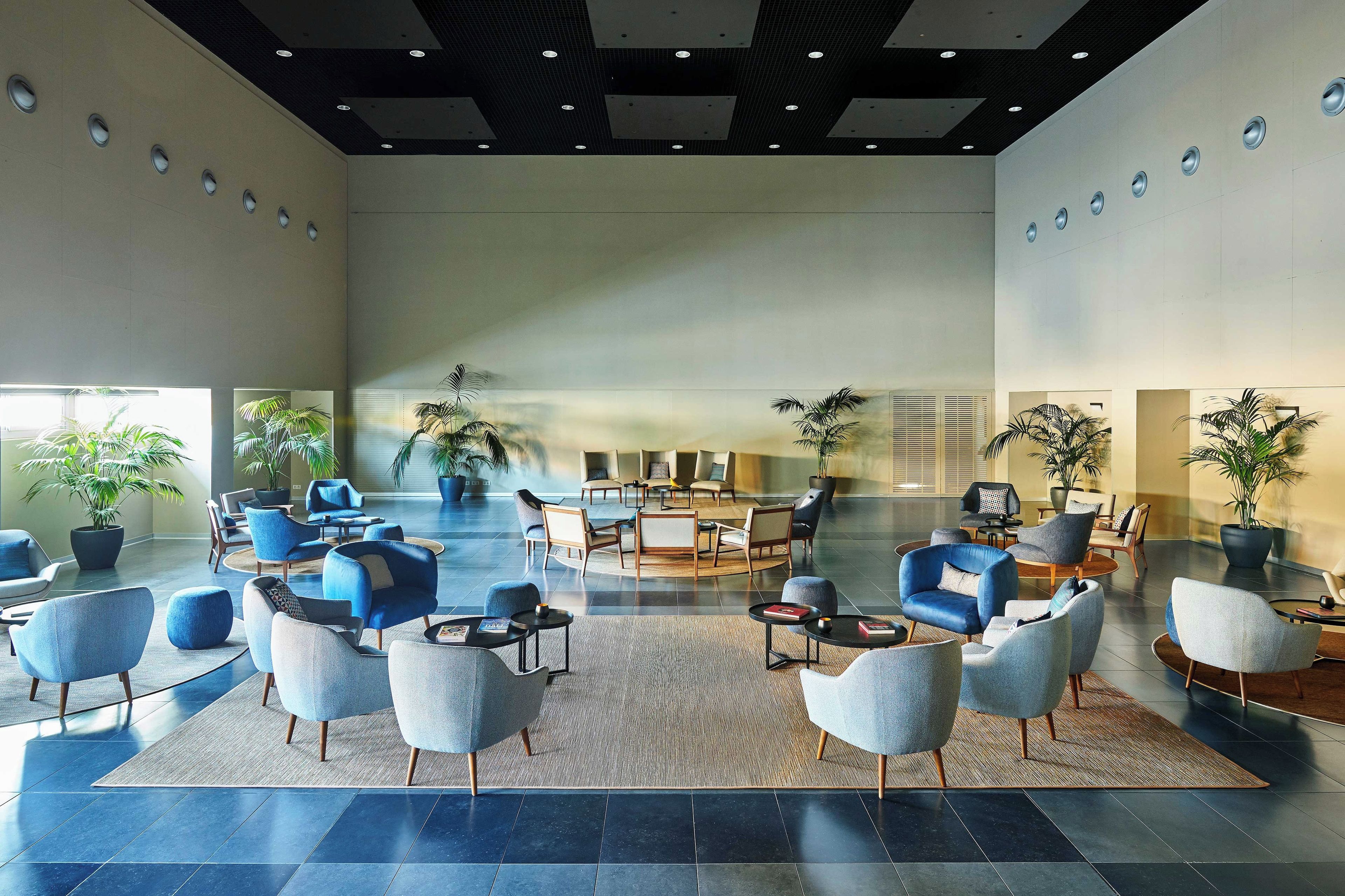 A spacious lobby with modern seating arrangements, a central coffee table, and potted plants.