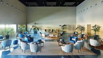 A spacious lobby with modern seating arrangements, a central coffee table, and potted plants.